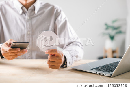 Feedback concept demonstrates positive customer satisfaction, person holds happy face with smartphone for online service evaluation, business quality rating Feedback concept demonstrates positive customer satisfaction, person holds happy face with smartphone for online service evaluation, business quality rating 136032728