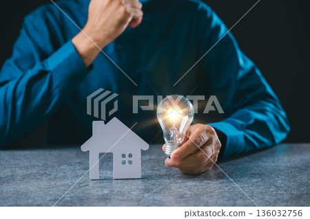 Real estate innovation showing white house model, glowing light bulb, energy savings, creative idea for home property, mortgage knowledge, businessman holding electricity solutions 136032756
