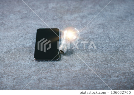 Glowing light bulb for digital marketing idea, modern business innovation concept beside mobile phone on grey stone surface shows creative market development and knowledge Glowing light bulb for digital marketing idea, modern business innovation concept beside mobile phone on grey stone surface shows creative market development and knowledge 136032760