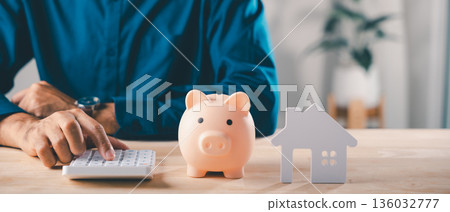Real estate money investment, piggy bank home saving, man uses calculator near small house model while planning finance to save, buying property through bank, mortgage insurance Real estate money investment, piggy bank home saving, man uses calculator near small house model while planning finance to save, buying property through bank, mortgage insurance 136032777