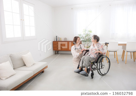 Caring for a wheelchair-bound mother at home. Wide-angle shot of the whole body as they look into each other's eyes and talk. 136032798