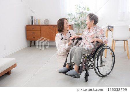 Caring for a wheelchair-bound mother at home. Wide-angle shot of the whole body as they look into each other's eyes and talk. Caring for a wheelchair-bound mother at home. Wide-angle shot of the whole body as they look into each other's eyes and talk. 136032799
