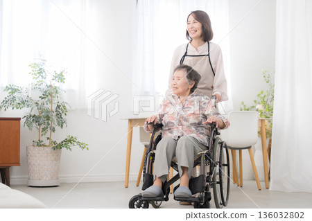 Caring for a wheelchair-bound mother at home. Wide-angle shot of the whole body as they look into each other's eyes and talk. 136032802