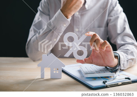 Hand holds large percent symbol calculating home property real estate mortgage loan interest rate for future investment house model on desk showing financial planning data Hand holds large percent symbol calculating home property real estate mortgage loan interest rate for future investment house model on desk showing financial planning data 136032863