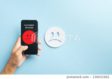 Survey shows customer online review mobile phone, hand holds smartphone with red unhappy feedback, poor service rating low satisfaction experience, white sad face visible Survey shows customer online review mobile phone, hand holds smartphone with red unhappy feedback, poor service rating low satisfaction experience, white sad face visible 136032882