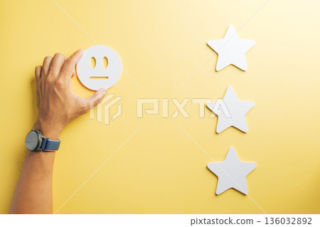 Hand holding neutral feedback icon next to three star symbols visually represents customer review and service rating for quality satisfaction, offering three point perspective on experience Hand holding neutral feedback icon next to three star symbols visually represents customer review and service rating for quality satisfaction, offering three point perspective on experience 136032892