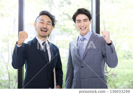 一位商人坐在漂亮的辦公室裡，透過翠綠的窗戶，他對著鏡頭揮拳大笑。這是一幅成就與成功的畫面。 136033299