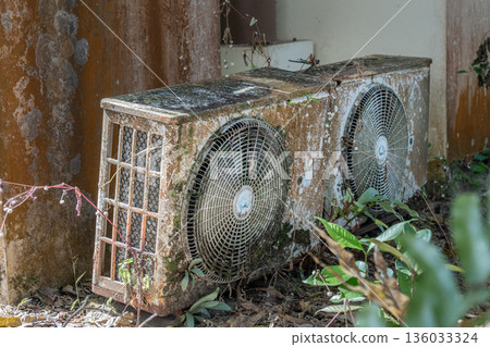 The old rusty and overgrown outdoor unit of the split air conditioning system. It is heavily corroded and covered with moss and dirt. timely maintenance of air conditioners and repairs. High quality The old rusty and overgrown outdoor unit of the split air conditioning system. It is heavily corroded and covered with moss and dirt. timely maintenance of air conditioners and repairs. High quality 136033324