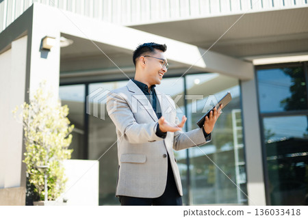 Businessman enjoying coffee break, smiling while checking smartphone messages outdoors, showing confidence and success in modern business lifestyle. Businessman enjoying coffee break, smiling while checking smartphone messages outdoors, showing confidence and success in modern business lifestyle. 136033418