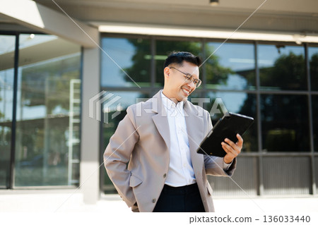 Happy businessman raising fist and cheering with smartphone in hand, celebrating success and victory with excitement and joy outdoors. Happy businessman raising fist and cheering with smartphone in hand, celebrating success and victory with excitement and joy outdoors. 136033440