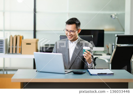 Asian man using laptop and tablet while sitting at her working place. Concentrated at work. Asian man using laptop and tablet while sitting at her working place. Concentrated at work. 136033446