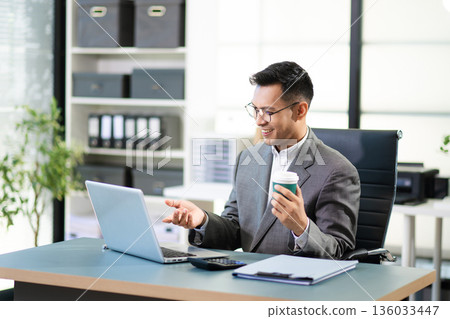Asian man using laptop and tablet while sitting at her working place. Concentrated at work. Asian man using laptop and tablet while sitting at her working place. Concentrated at work. 136033447