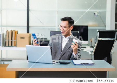 Asian man using laptop and tablet while sitting at her working place. Concentrated at work. Asian man using laptop and tablet while sitting at her working place. Concentrated at work. 136033450