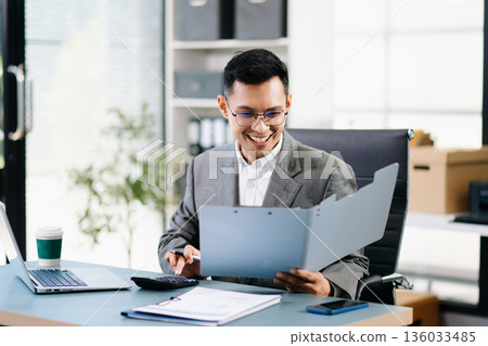 Asian man using laptop and tablet while sitting at her working place. Concentrated at work. 136033485