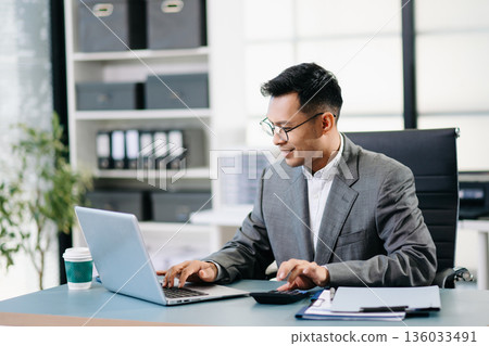 Asian man using laptop and tablet while sitting at her working place. Concentrated at work. 136033491