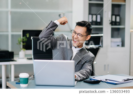 businessman celebrating success after receiving good news on his smartphone in a modern office, expressing joy and achievement 136033493