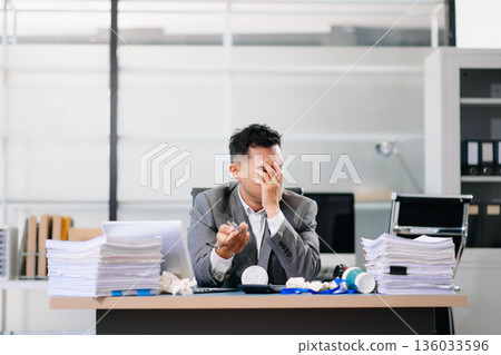 Exhausted businessman holding coffee cup at desk, feeling tired and overworked with paperwork and deadlines in modern office environment. 136033596