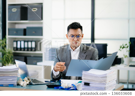 Focused office worker analyzing documents, reviewing business reports with stress and concentration in workplace setting. Focused office worker analyzing documents, reviewing business reports with stress and concentration in workplace setting. 136033608