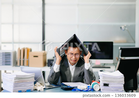 Focused office worker analyzing documents, reviewing business reports with stress and concentration in workplace setting. 136033609