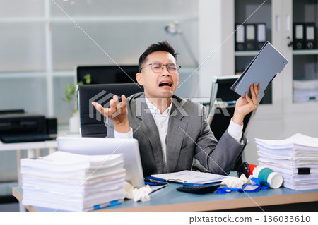 Focused office worker analyzing documents, reviewing business reports with stress and concentration in workplace setting. 136033610