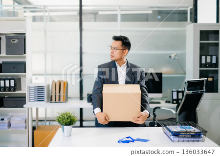 Sad businessman sitting in office with box and ID card after layoff, feeling exhausted and depressed from job loss and workplace stress. 136033647