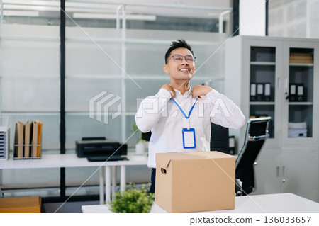 Asian office worker packing belongings into a cardboard box, representing resignation, job change, or a fresh career start in a modern workplace environment. Asian office worker packing belongings into a cardboard box, representing resignation, job change, or a fresh career start in a modern workplace environment. 136033657