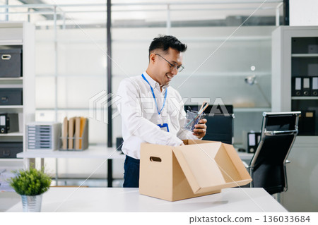 Asian businessman smiling while reading documents in a modern office. business, workplace, productivity, and positive professional lifestyle. Asian businessman smiling while reading documents in a modern office. business, workplace, productivity, and positive professional lifestyle. 136033684
