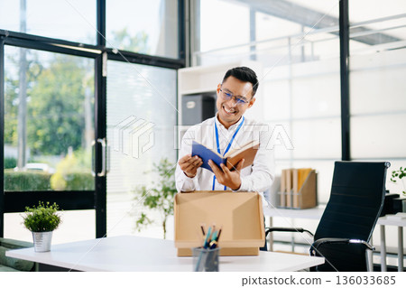 Asian businessman smiling while reading documents in a modern office.  business, workplace, productivity, and positive professional lifestyle. 136033685