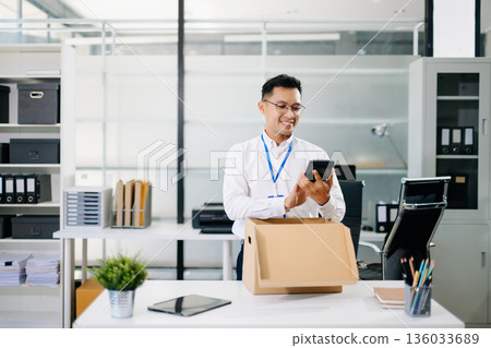 Asian businessman smiling while reading documents in a modern office. business, workplace, productivity, and positive professional lifestyle. Asian businessman smiling while reading documents in a modern office. business, workplace, productivity, and positive professional lifestyle. 136033689