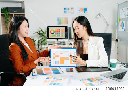 Two professional women designers discussing UX UI and color palette in a creative modern office. Ideal for teamwork, innovation 136033921