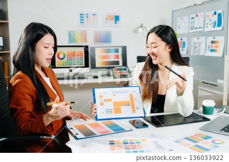 Two professional women designers discussing UX UI and color palette in a creative modern office. Ideal for teamwork, innovation 136033922