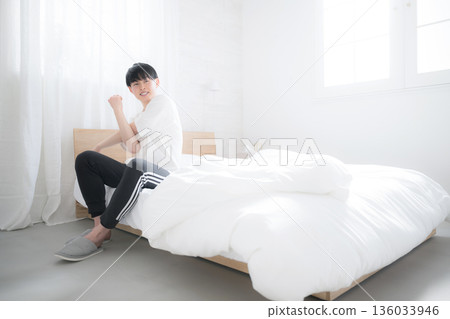 A young man waking up in bed bathed in the morning sun stretching his arms A young man waking up in bed bathed in the morning sun stretching his arms 136033946