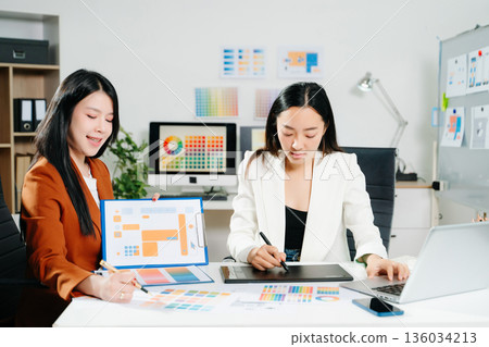 Two professional women designers discussing UX UI and color palette in a creative modern office. Ideal for teamwork, innovation 136034213