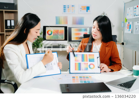 Two creative female designers discussing color palettes and UX UI project in a modern office. Perfect for teamwork, innovation, and digital design themes. 136034220