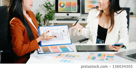 Two creative female designers discussing color palettes and UX UI project in a modern office. Perfect for teamwork, innovation, and digital design themes. 136034305