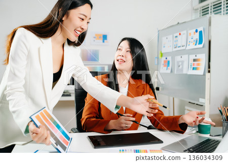 Two creative female designers discussing color palettes and UX UI project in a modern office. Perfect for teamwork, innovation, and digital design themes. Two creative female designers discussing color palettes and UX UI project in a modern office. Perfect for teamwork, innovation, and digital design themes. 136034309