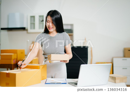 Startup small business SME, Entrepreneur owner woman using smartphone or tablet taking receive and checking online purchase shopping order to preparing pack product box. 136034316
