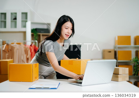 Startup small business SME, Entrepreneur owner woman using smartphone or tablet taking receive and checking online purchase shopping order to preparing pack product box. Startup small business SME, Entrepreneur owner woman using smartphone or tablet taking receive and checking online purchase shopping order to preparing pack product box. 136034319