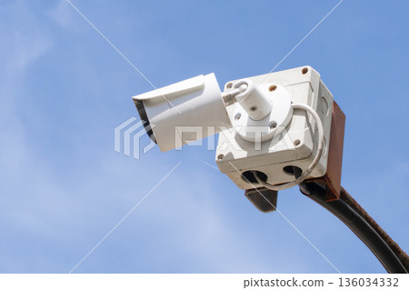 A white CCTV surveillance camera on an outdoor street against a background of blue sky in close-up. Security and surveillance, monitoring of the street situation in a criminal area. High quality photo 136034332