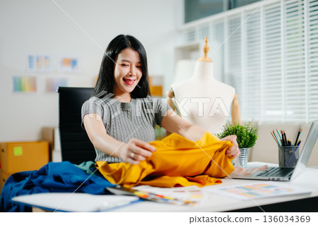 Asian fashion designer working in studio with mannequin, fabric and laptop. Creative fashion business, tailor planning clothing design Asian fashion designer working in studio with mannequin, fabric and laptop. Creative fashion business, tailor planning clothing design 136034369