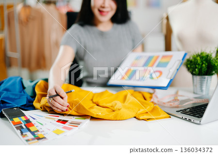 Asian fashion designer working in studio with mannequin, fabric and laptop. Creative fashion business, tailor planning clothing design Asian fashion designer working in studio with mannequin, fabric and laptop. Creative fashion business, tailor planning clothing design 136034372