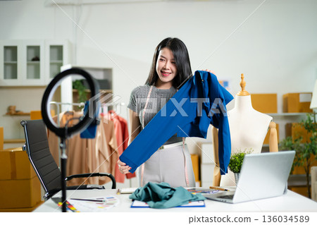 Fashion designer working in a studio with laptop and color palettes. Creative digital design process, textile planning, branding development 136034589