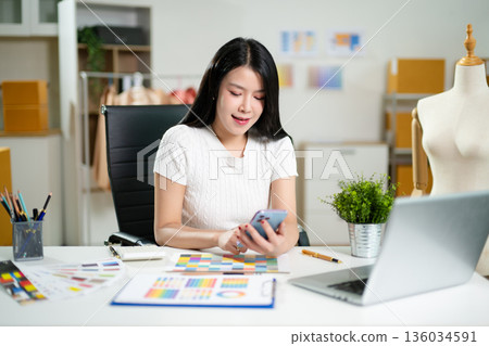 Fashion designer working in a studio with laptop and color palettes. Creative digital design process, textile planning, branding development 136034591