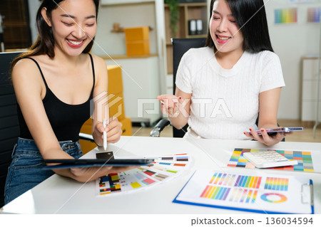 Fashion designers working together in a studio with color palettes, tablet, and sketches. Creative teamwork, modern workspace, textile planning 136034594