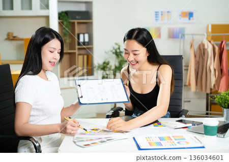 Fashion designers collaborating with sketches and color palettes in a studio. Creative design process, textile planning, branding development, and fashion concept. 136034601