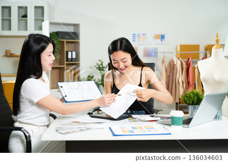 Fashion designers collaborating with sketches and color palettes in a studio. Creative design process, textile planning, branding development, and fashion concept. 136034603