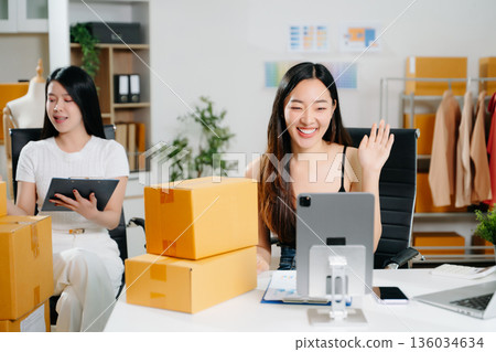 Startup small business SME, Entrepreneur owner woman using smartphone or tablet taking receive and checking online purchase shopping order to preparing pack product box. 136034634