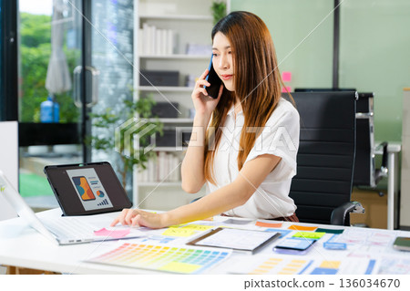 Creative Asian UX UI designer planning mobile app layout with sticky notes, color swatches, and wireframes. 136034670