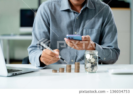 businessman holding coins putting in glass with using smartphone and calculator to calculate concept saving money 136034753