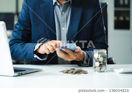 businessman holding coins putting in glass with using smartphone and calculator to calculate concept saving money 136034828